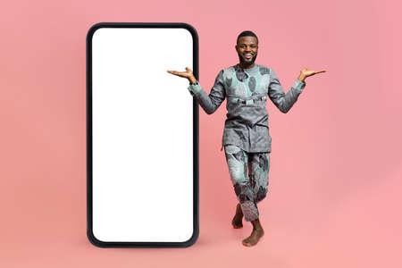 African american man in traditional costume dancing near big blank smartphone, demonstrating copy space for adの写真素材