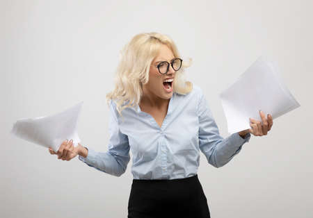 Stressed young businesswoman with papers feeling angry or having nervous breakdown, standing over light backgroundの写真素材