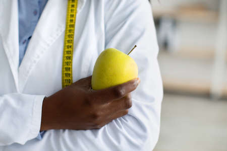 An apple a day and a virus away. Green fresh apple in black female doctor hand, nutritionist posing with measuring tapeの写真素材