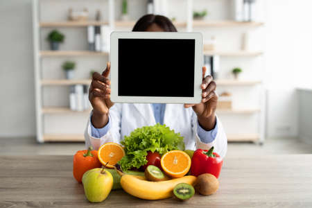 Black nutritionist holding digital tablet with blank screen, demonstrating mockup for website or app designの写真素材