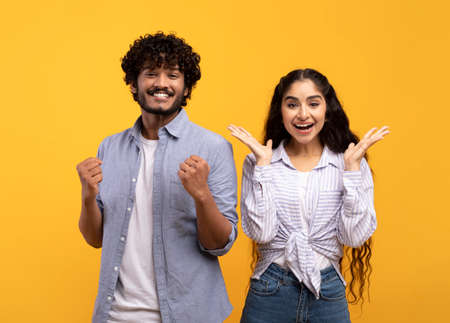 Wow. Overjoyed indian spouses gesturing in amazement looking at camera over yellow studio backgroundの写真素材