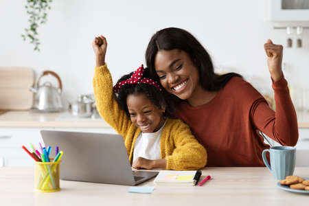 Joyful Black Mother And Little Daughter Celebrating Success With Laptop At Homeの写真素材