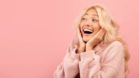 Wow offer. Amazed lady with open mouth touching her cheeks with hands and looking at copy space over pink backgroundの写真素材