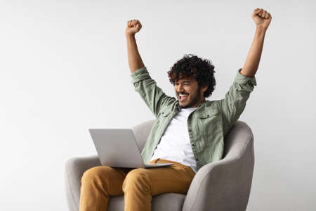 Happy indian man with laptop raising hands upの写真素材