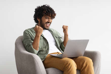 Emotional hindu guy with laptop celebrating success, copy spaceの写真素材