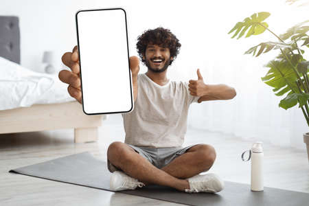 Cheerful sporty indian guy showing smartphone with empty screen