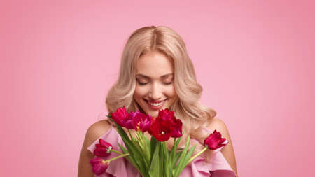 Happy Blonde Female Holding Bouquet Of Tulips Over Pink Backgroundの写真素材