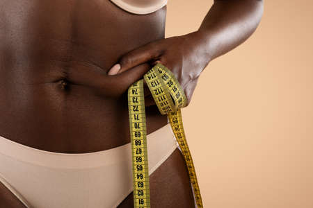 Cropped of black woman in underwear pulling skin on belly