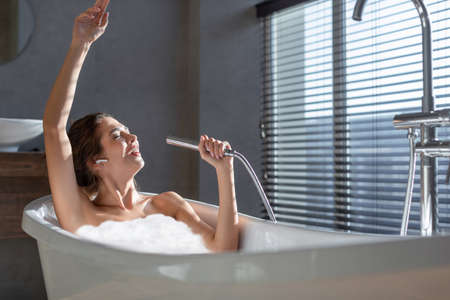 Happy Cheerful Young Woman Relaxing In Foamy Bathtub And Singing