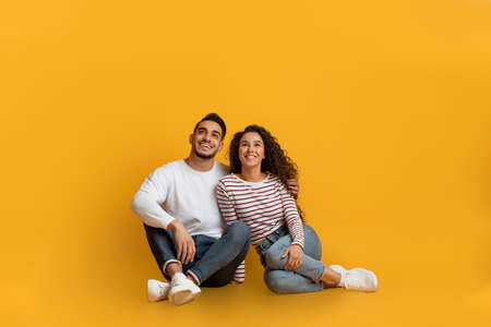 Dreamy Young Arab Couple Sitting On Floor And Looking At Copy Space