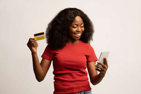 Online Shopping. Cheerful Young Black Female Using Smartphone And Credit Card