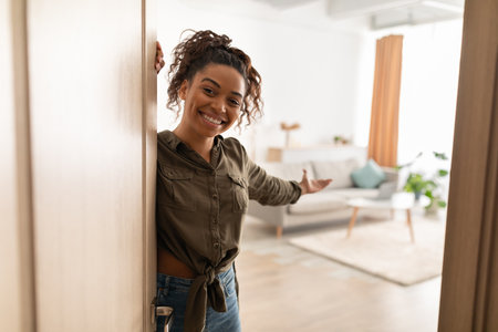 Joyful Millennial Black Lady Opening Door Welcoming Standing At Homeの写真素材