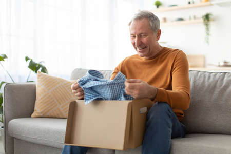 Happy mature man unpacking parcel after online shopping