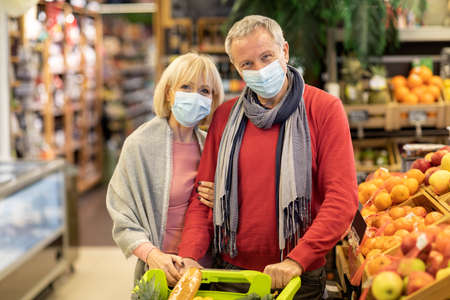 Elderly couple in face masks posing with shopping cartの写真素材