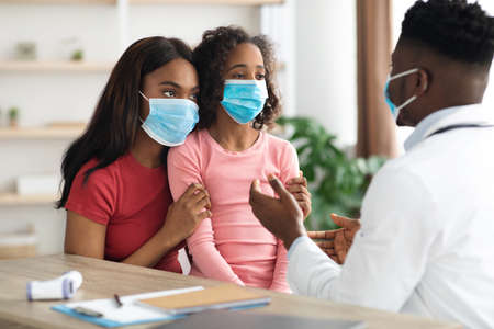 Sick daughter and mother in face masks visiting pediatricianの写真素材