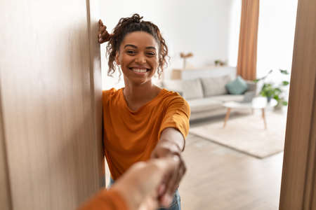 Cheerful African Woman Shaking Hands In Opened Door At Home
