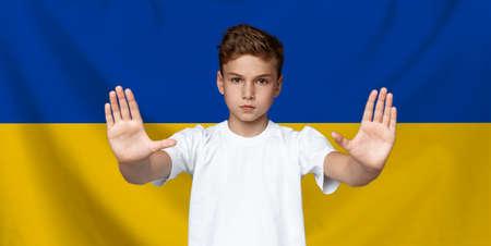 Teenage boy making stop gesture over yellow blue Ukrainian flag backgroundの写真素材