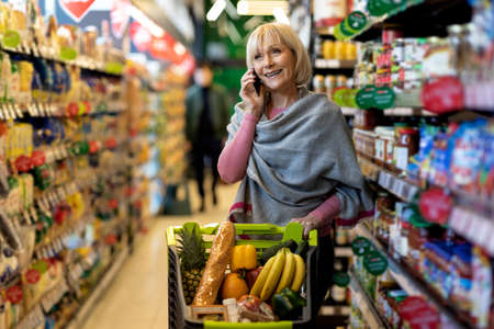 Positive senior woman having phone conversation while shoppingの写真素材