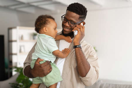 Black father talking on phone and holding baby on handsの写真素材