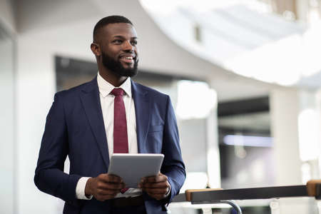 Cheerful black manager with digital tablet walking by office building