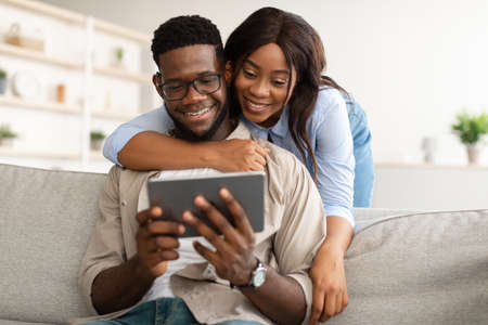 African american couple sitting on sofa, using tabletの写真素材