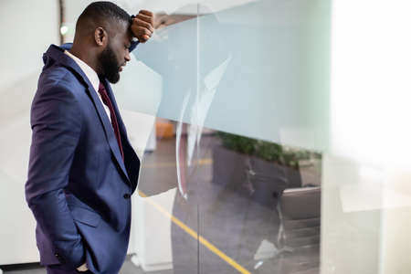 Exhausted black businessman leaning on window glassの写真素材