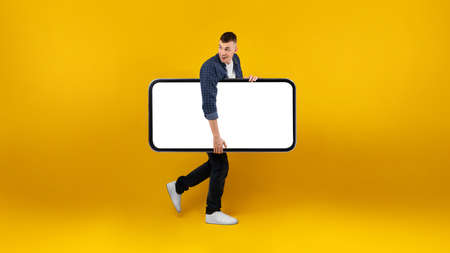 Guy Carrying Big Phone With Blank Screen Over Yellow Background