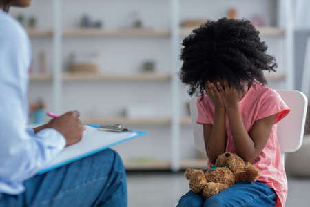 Upset little black kid crying at psychotherapy sessionの写真素材