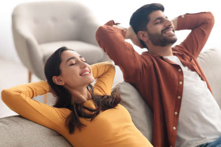 Relaxed Middle Eastern Spouses Sitting On Sofa Relaxing At Homeの写真素材