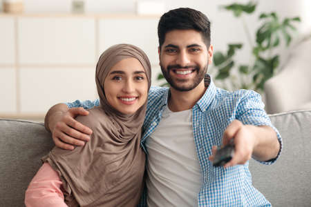 Happy Middle Eastern Couple Watching Television Switching Channels At Home