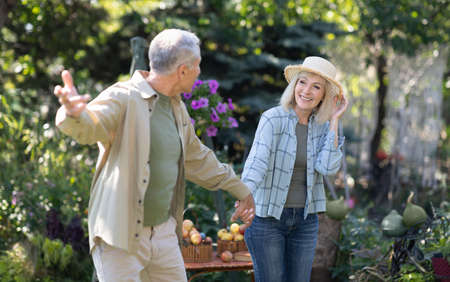 Happy loving senior couple holding hands and walking in their garden on warm spring day, enjoying time togetherの写真素材