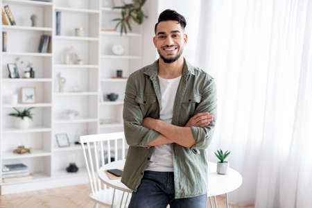 Handsome Young Arab Guy Standing With Folded Arms Near Desk At Homeの写真素材