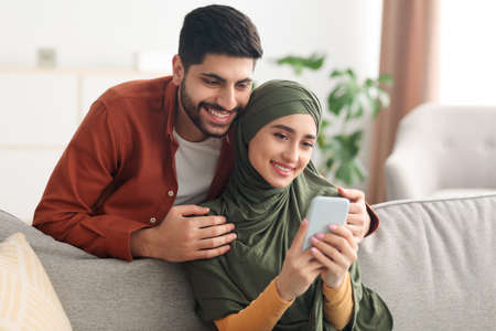 Happy Arabic Couple Using Smartphone With New Application At Homeの写真素材