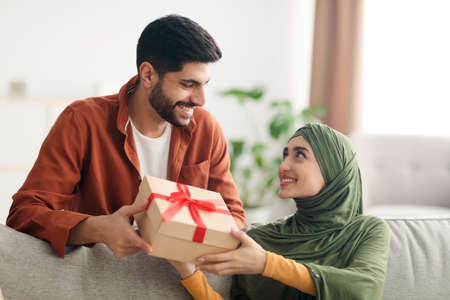 Muslim Husband Giving Present Box To Happy Wife Sitting Indoorsの写真素材
