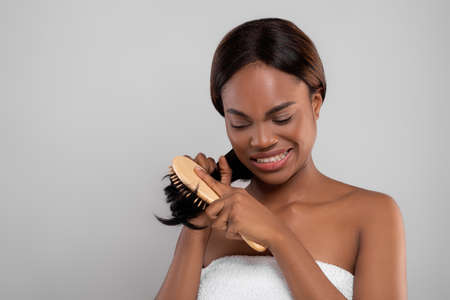 Unhappy Black Female Combing Her Tangled Hair With Bamboo Brush
