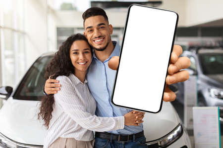 Loving muslim family showing smartphone with blank screen, buying carの写真素材