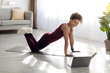 Attractive sporty black woman exercising at home, using laptop