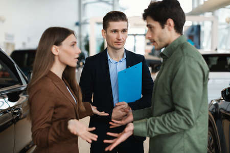 Millennial Caucasian couple having argument while communicating to car salesman at auto dealership