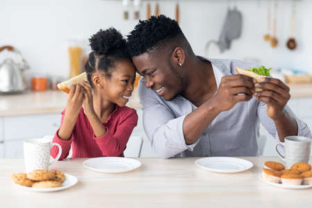 Loving african american girl cuddling with daddy while having breakfastの写真素材