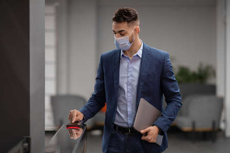 Middle eastern guy in face mask employee entering security codeの写真素材