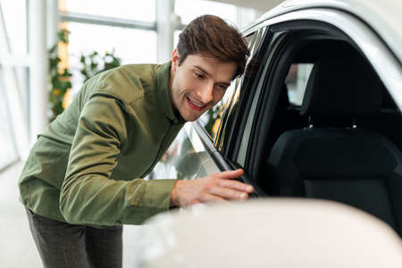 Happy young guy touching his new car, excited about buying automobile at dealership centre, copy spaceの写真素材