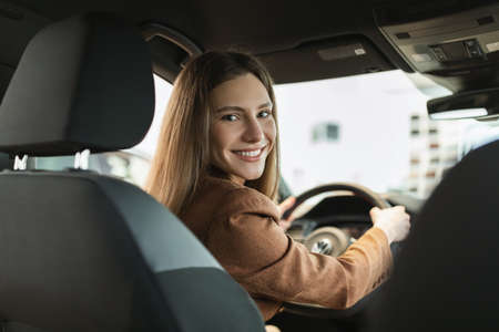 Happy young Caucasian woman buying new car, doing test drive, sitting inside modern luxury auto at...