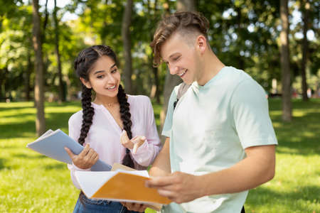 Happy diverse students studying with books, preparing for classes while walking in university campus outdoorsの写真素材