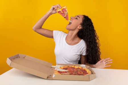 Happy Latin Lady Biting Pizza Sitting At Table