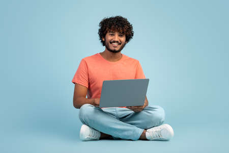 Handsome indian man using modern laptop on blue