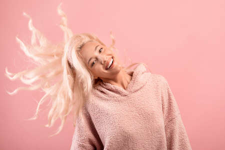 Happy blonde lady with shiny flying hair having fun and smiling at camera, posing over pink studio backgroundの写真素材
