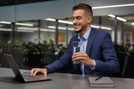 Healthy arabic businessman drinking water while working on laptopの写真素材
