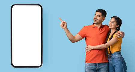 Mobile Ad. Excited arab couple pointing aside at big blank smartphone screenの写真素材