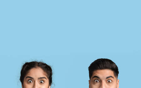 Cropped Shot Of Shocked Young Arab Couple Peeking Out Over Blue Backgroundの写真素材