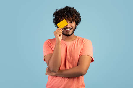 Curly indian guy covering eye with credit cardの写真素材